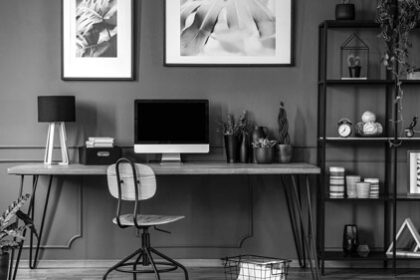 Posters on grey wall above wooden desk in natural home office interior with plants and lamp