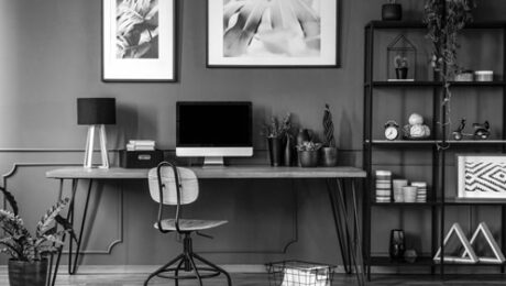 Posters on grey wall above wooden desk in natural home office interior with plants and lamp